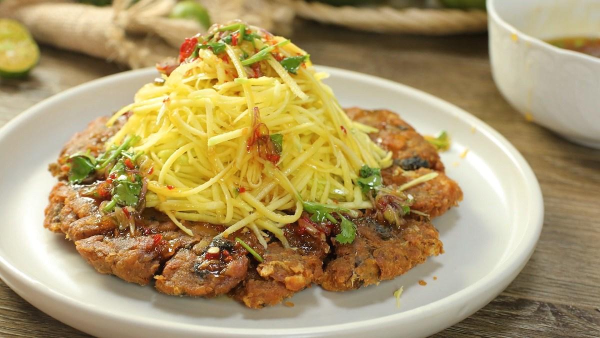 Chảo dầu nóng đang chiên những miếng chả cá tròn dẹt vàng ruộm cho món bún chả cá