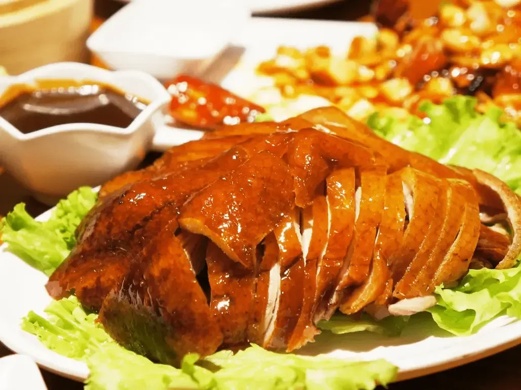 Đĩa vịt quay thành phẩm đã chặt miếng đẹp mắt, da vàng nâu giòn rụm, thịt hồng hào, bày trên đĩa trắng cùng rau thơm